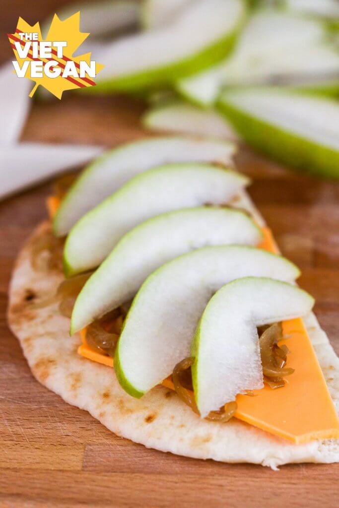 Sliced pear layered on top of caramelized onions, vegan cheese, and half moon of naan bread