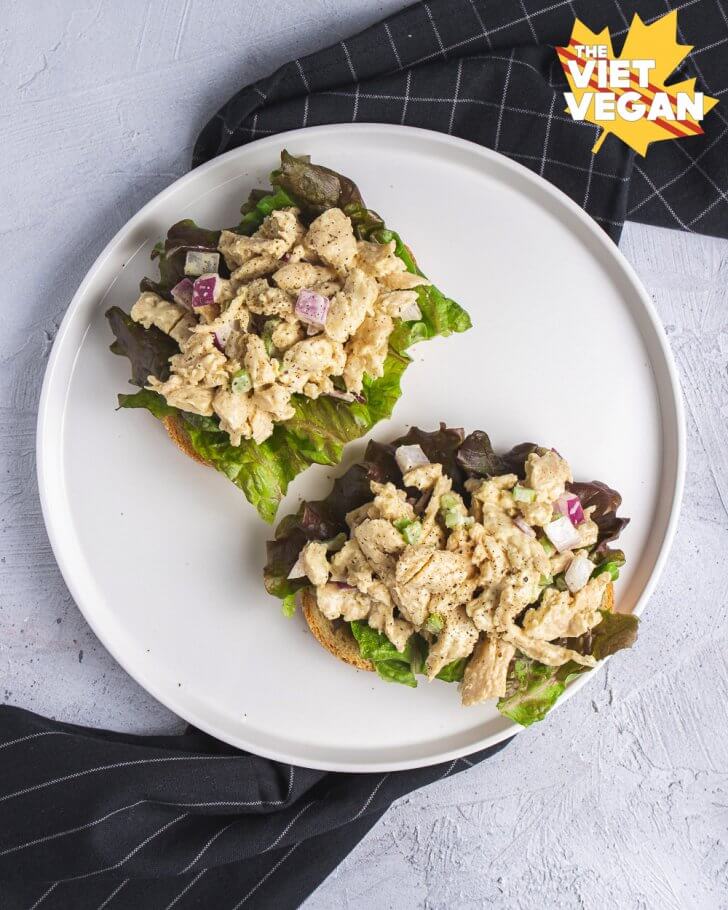 Two vegan chicken salad open faced sandwiches, on a plate with a napkin shot from above