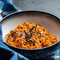 red ramen noodles topped with sesame and nori in a bowl, set on a blue kitchen cloth on a black surface, from the front
