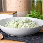 finished cilantro rice in a bowl on a tea towel with cilantro and garlic