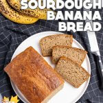 vegan sourdough banana bread, sliced and displayed on a white plate, on a black grid-patterned tea towel, with overripe bananas and a bread knife
