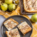 Three slices of the tart on a plate, on a yellow tea towel with the baked tart in the background and green California Bartlett pears beside them