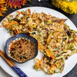 Text overlay on a photo of Vegan vegetable fritters on a plate with dipping sauce, surrounded by autumn flowers (dahlias)