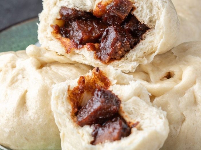 A plate of vegan char siu bao buns with one split open to reveal the char siu seitan inside
