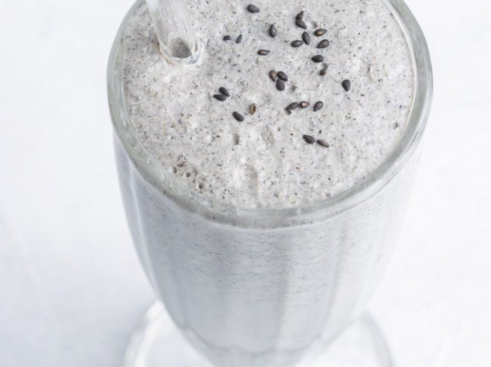 black sesame milkshake in large milkshake glass with a glass straw, garnished with black sesame seeds