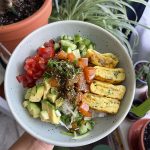 Vegan poke bowl filled with tomatoes, avocado, vegan salmon poke, cucumber, and vegan tamagoyaki over a bed of rice