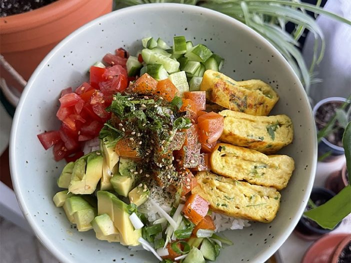 Vegan poke bowl filled with tomatoes, avocado, vegan salmon poke, cucumber, and vegan tamagoyaki over a bed of rice