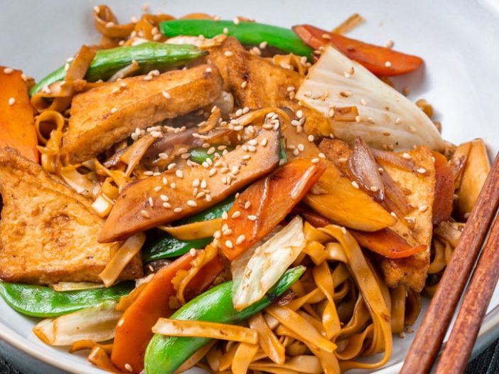 Vietnamese stir fried chow mein (mi xao chay) in a bowl with chopsticks on a dark surface