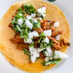 carne asada tacos made with soy curls on a yellow corn tortilla topped with onion cilantro relish