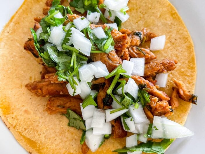 carne asada tacos made with soy curls on a yellow corn tortilla topped with onion cilantro relish