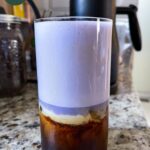 a glass of vietnamese iced coffee with a layer of oat cream and ube foamed milk