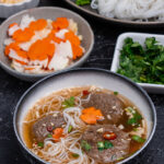 bowl with dipping sauce, with impossible chả chay, noodles, and toppings in the bowl, Bowls of the toppings in the background