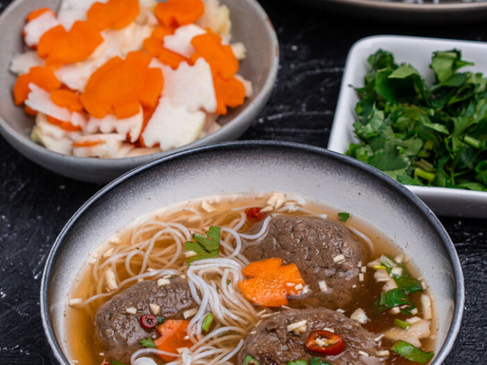 bowl with dipping sauce, with impossible chả chay, noodles, and toppings in the bowl, Bowls of the toppings in the background