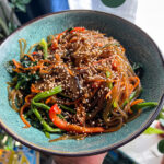 japchae noodles in a green bowl with sesame seeds on top