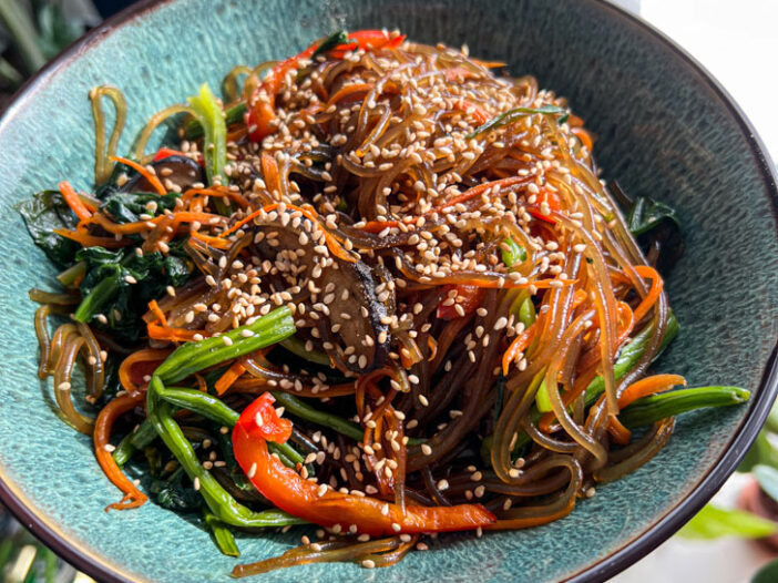 japchae noodles in a green bowl with sesame seeds on top