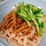 sesame udon topped with sliced seitan, cucumber, and green onion curls