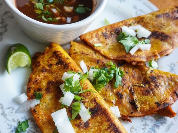 vegan birria tacos with soy curls plated with onion and cilantro with consomme