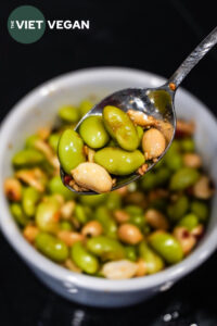 edamame peanut in a soy sauce based dressing in a spoon over a bowl