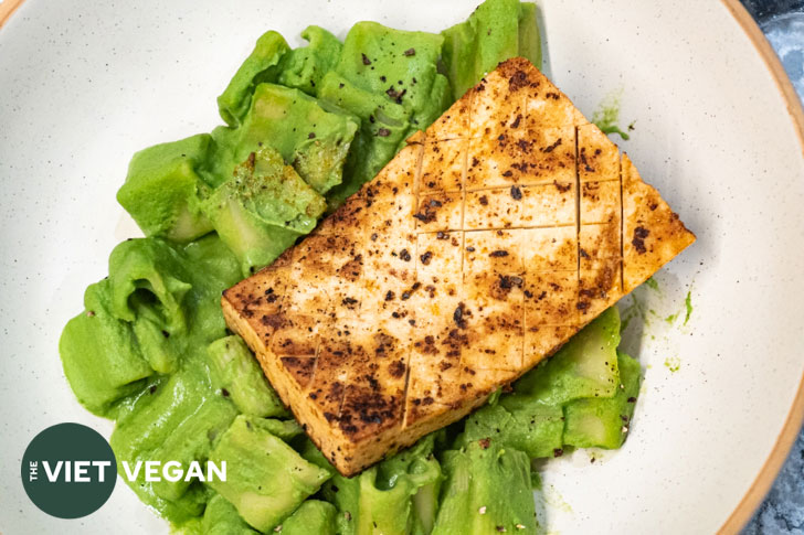 close up of quick easy tofu steak on a bed of green creamy pasta on a speckled cream plate