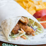 A vegan chicken curry salad wrap on a plate with some chips and apple slices