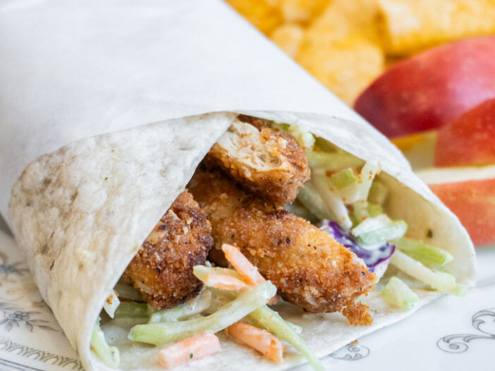 A vegan chicken curry salad wrap on a plate with some chips and apple slices