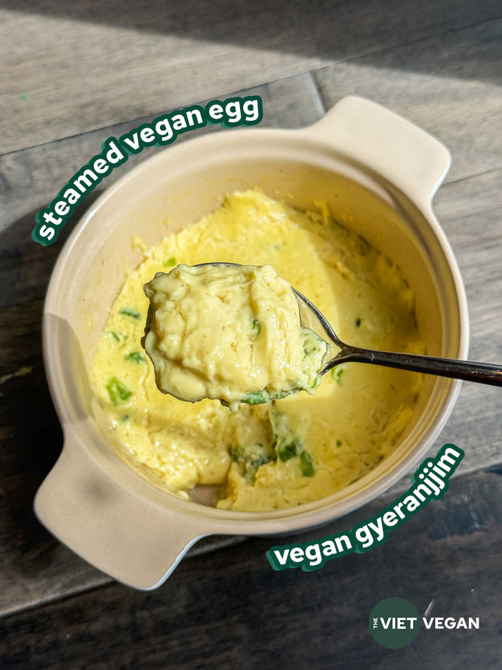 a scoop of the steamed vegan egg in a spoon over a casserole dish of the rest of the steamed egg